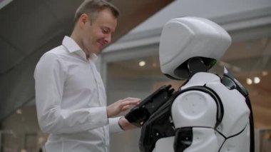 Alışveriş merkezindeki adam bir robot danışmanla iletişim kuruyor. Modern dükkan ve robot satıcısı. Robot Alışveriş Merkezi'nde bir adam yardımcı olur