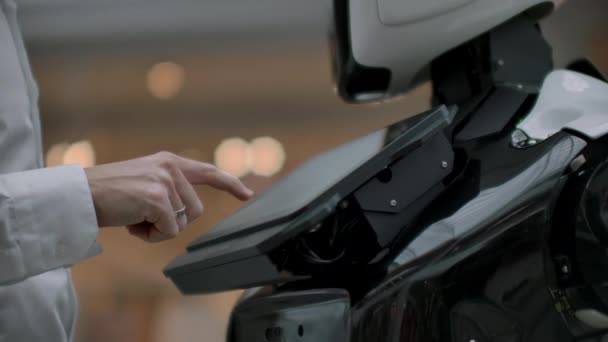 Un uomo in camicia comunica con un robot bianco facendo domande e premendo lo schermo con le dita . — Video Stock