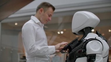 Alışveriş merkezindeki adam bir robot danışmanla iletişim kuruyor. Modern dükkan ve robot satıcısı. Robot Alışveriş Merkezi'nde bir adam yardımcı olur
