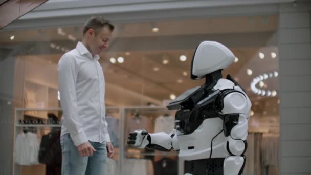 Mężczyzna w koszulce komunikuje się z białym robotem zadając pytania i naciskając ekran palcami. — Wideo stockowe