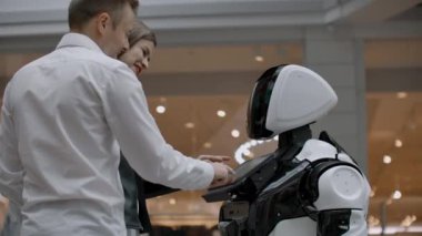İki kişi bir erkek ve bir kadın bir robotile iletişim kurar. Elleriniz ekranda robota basın. Bir robot asistanı bir çift ile bir alışveriş merkezinde etkileşim.