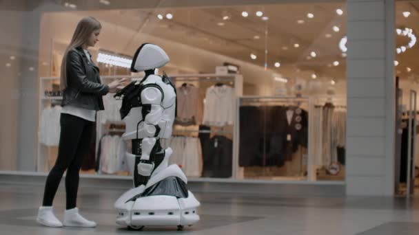 Una programadora femenina prueba el robot para la capacidad de interactuar con los usuarios. El uso de un robot asistente en la oficina. El robot ayuda a la chica . — Vídeos de Stock