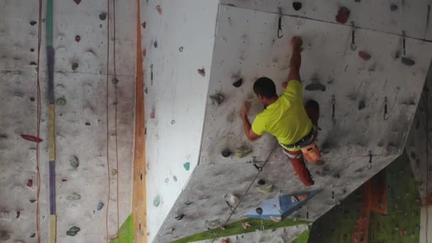 Il giovane arrampicatore sta scalando la palestra di arrampicata Inside. sottile grazioso uomo esercizio a indoor climbing palestra parete — Video Stock