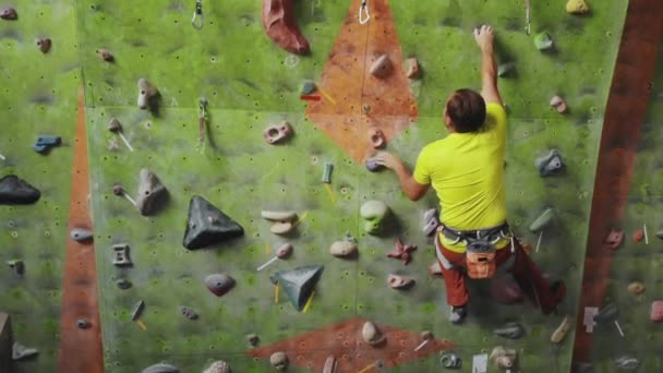 Mannelijke klimmer klimt de klif muur in de kamer bereiken en aangrijpende hold. Een professionele geconcentreerde klimmer beweegt de muur, de camera stijgt en legt zijn bewegingen neer. Boom volgcamera — Stockvideo