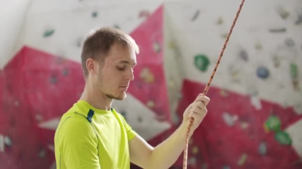 Porträt des schönen Mannes Bergsteiger, der einen anderen Bergsteiger mit Seil abstützt. drinnen künstliche Kletterwand und Ausrüstung — Stockvideo