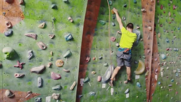 Erkek dağcı odanın uçurum duvarına tırmanıyor. Profesyonel konsantre dağcı duvara doğru hareket eder, kamera yükselir ve hareketlerini bırakır. Boom kamera izle — Stok video