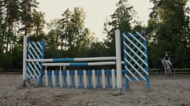 Ağır çekim, Close Up, düşük açı: Horsegirl güneşli açık havada kumlu parkour terbiye arenada çit atlama güçlü kahverengi at binme. Rekabetçi binici modacı engellerin üzerinden atlama eğitimi.