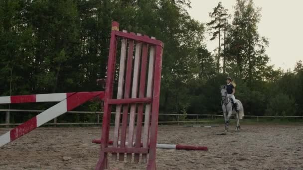 En kvinna jockey i en svart och vit kostym på en häst gör ett hopp över barriären. Slow motion: en kvinna jockey i en svart och vit kostym på en häst gör ett hopp. — Stockvideo