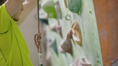 Ellerini tebeşirlemek ve yavaş çekimde sigorta ile duvara tırmanmak için salonda duvara tırmanmaya hazırlanıyor bir dağcı portresi