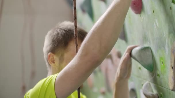 Il giovane arrampicatore sta scalando la palestra di arrampicata Inside. sottile grazioso uomo esercizio a indoor climbing palestra parete — Video Stock