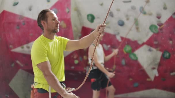 Man belaying another climber with rope. Top view of young athletic man belaying and watching another climber with rope. Summer time. Climbing equipment — Stock Video