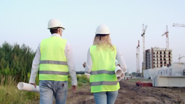 Volver convertido en ingeniero y técnico en el sitio de construcción revisando planos de oficina y dibujos técnicos caminar y discutir — Vídeo de stock