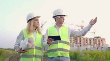 Yetişkin mühendis erkek ve mimar kadın operasyonda bir tablet kullanır. İleti yazar veya çizimi denetler. Arka plana karşı bina.