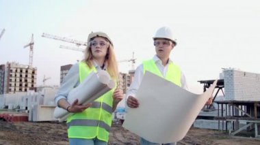 İnşaatçı ve mimar erkek ve kadın inşaat alanı yakınında duran modern iş merkezinin inşaat planı tartışıyorlar. Binaya gidiyorlar.