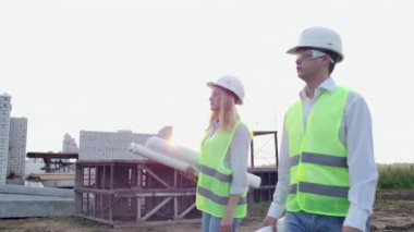 Erkek ve kadın süpervizör ve beyaz kask çizimleri ile asistan gidin ve nesnelerin yerini gösteren şantiyede konuşmak