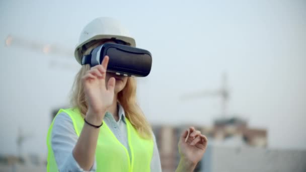 Ritratto di un'ispettore donna che analizza il lavoro dei costruttori utilizzando occhiali di realtà virtuale. Una donna con un casco e un giubbotto protettivo sta in occhiali VR e muove le mani — Video Stock