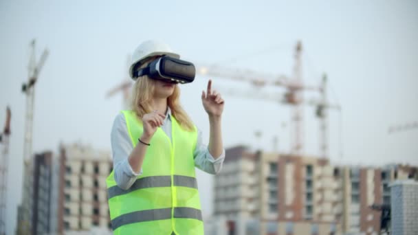 Портрет женщины-инспектора, анализирующей работу строителей с использованием очков виртуальной реальности. Женщина в шлеме и защитном жилете стоит в очках и двигает руками. — стоковое видео