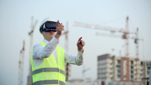 Ritratto di un ispettore maschio che analizza il lavoro dei costruttori utilizzando occhiali di realtà virtuale. Un uomo con un casco e un giubbotto protettivo sta in occhiali VR e muove le mani — Video Stock