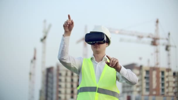 Человек в очках виртуальной реальности шлем и жилет на фоне конструкции контролирует руки интерфейса и проверяет качество строительства и развития — стоковое видео