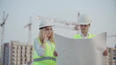 Kadın telefonda konuşuyor ve inşaat aşamasında binaların arka planda duran çizimler üzerinde ne olduğunu Builder sorar