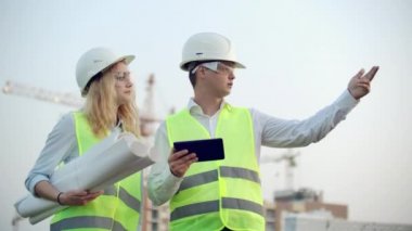 Mühendislerin iki meslektaşı bir adam ve bir kadın inşaat ve vinçler altında binaların arka planda bir çizim ve tablet bilgisayar tartışırken, bir kadın patron ile telefonda konuşurken.