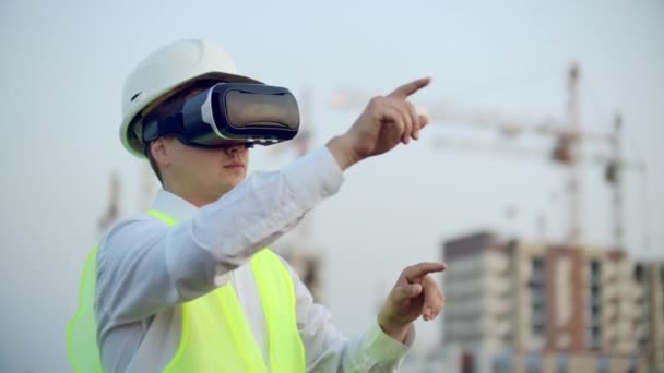 Portrait d'un inspecteur qui analyse le travail des constructeurs à l'aide de lunettes de réalité virtuelle. Un homme avec un casque et un gilet de protection se tient dans des lunettes VR et bouge les mains — Video