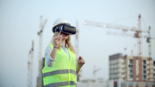 Porträt einer Kranführerin, die mit einer Virtual-Reality-Brille eine Baustelle bedient. Bauleiterin steuert Baufortschritt und -plan mit Gesten bei Sonnenuntergang — Stockvideo