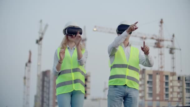 Zwei Inspektoren der Zukunft auf der Baustelle nutzen Virtual-Reality-Brille auf dem Hintergrund von Gebäuden und Kränen. — Stockvideo
