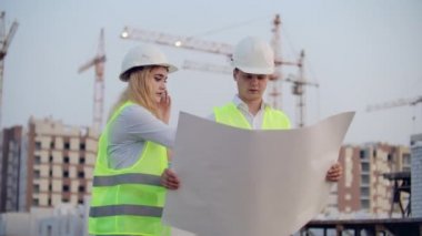 Kadın telefonda konuşuyor ve inşaat aşamasında binaların arka planda duran çizimler üzerinde ne olduğunu Builder sorar