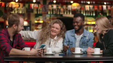 Bir adam arkadaşlarına akıllı telefonunda komik sarmaşıklar gösterir. Bir arkadaş şirketi, dört arkadaştan oluşan çok ırklı çok uluslu bir şirket olan telefon ekranına bakarken fotoğraf ve videoları tartışıyor.