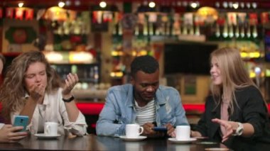 Mutlu çeşitli arkadaşları birlikte akıllı telefonda komik online video izlerken gadget ile eğlenmek, çok kültürlü genç arkadaşlar telefon konuşurken gülen toplantı da mobil uygulamalar kullanın masada oturun.