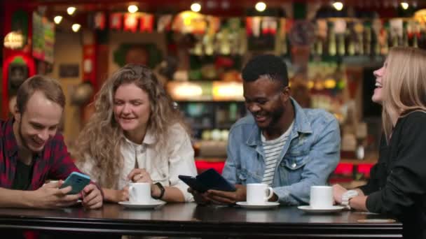 Bir restoranda arkadaş neşeli bir şirket akıllı telefonlar ve gülmek fotoğrafları tartışmak — Stok video