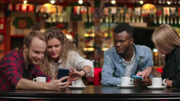 Les couples multiethniques assis dans un café regardent les écrans par téléphone et feuillettent les photos dans la bande téléphonique — Video