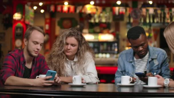 Zwei Männer und zwei Frauen multiethnische Paare sitzen in einem Café und schauen auf die Bildschirme von Smartphones und diskutieren — Stockvideo