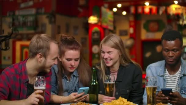 Een man en twee meisjes zitten in een bar en kijken naar het telefoon scherm terwijl in het gezelschap van vrienden — Stockvideo