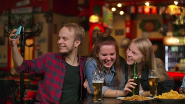 Groep vrienden man en twee meisjes nemen selfie in een bar lachen en glimlachen. Tijd doorbrengen met dumbfounds in een bar. — Stockvideo