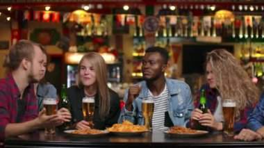 Çok ırklı grappa arkadaşlar bir barda bira içme ve cips yerken sohbet eğlenmek oturuyor