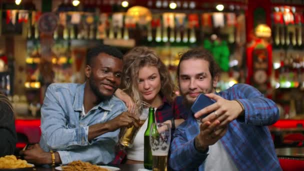 African American z europejskimi przyjaciółmi siedzi w barze bierze selfie. Duża grupa przyjaciół siedzi w barz przy jednym stole na czacie, picie piwa i robienia zdjęć — Wideo stockowe