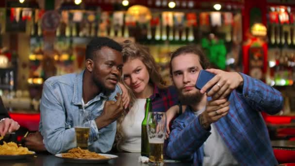 Tres amigos, dos europeos y hombres afroamericanos son fotografiados juntos mientras están sentados en un bar de cerveza. Empresa multinacional de amigos — Vídeos de Stock