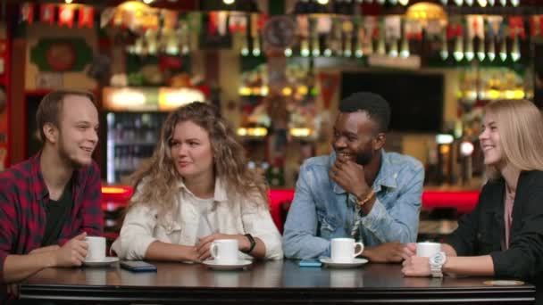 Uma empresa multinacional de amigos estudantes bebe café e fala em um restaurante. Quatro amigos conversando rindo e sorrindo — Vídeo de Stock