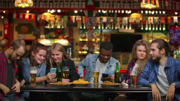 Ομάδα φίλων των φοιτητών μπαρ πίνουν μπύρα και να δούμε τις οθόνες των smartphones χαμογελαστή — Αρχείο Βίντεο
