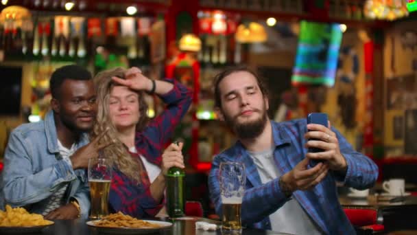 Grupo de amigos hombre y dos chicas tomar selfie en un bar riendo y sonriendo. Pasar tiempo con dumbfounds en un bar . — Vídeo de stock