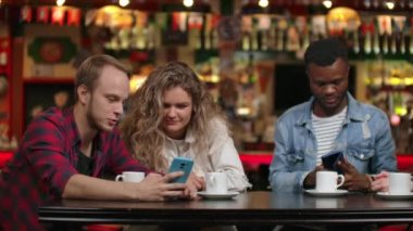 Bir barda bir grup arkadaş bir akıllı telefon ekranına bakarken kahve içme ve tartışıyor