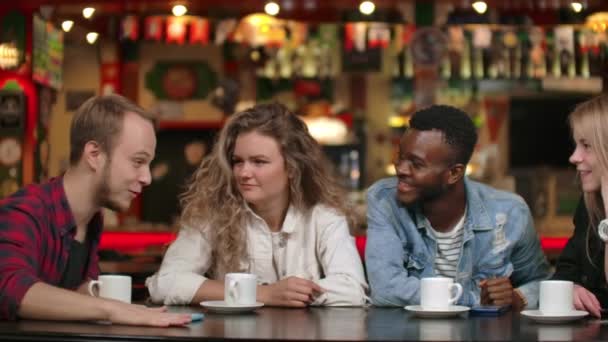 Een man in een shirt vertelt een verhaal aan vrienden, twee meisjes en een Afro-Amerikaan luisteren en lachen. Een groep vrienden tijd samen doorbrengen. Studenten vergadering — Stockvideo