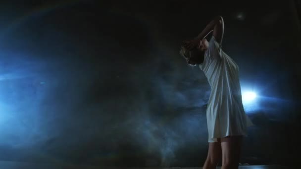 Zoom κάμερα μετακινείται γύρω από τη σκηνή με το λογισμικό και τον καπνό. Κορίτσι μπαλαρίνα χορεύει σε ένα λευκό φόρεμα γυρίζοντας πλαστικό, ενώ εκτελεί πιρουέτες και περιστροφές, βιώνει συναισθήματα — Αρχείο Βίντεο