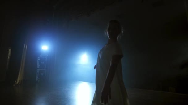 Збільшення камери переміщує жінку-танцюриста по сцені з програмним забезпеченням і димом. Сучасний драматичний балет, жінка в білій сукні обертається на одній нозі і стрибає . — стокове відео