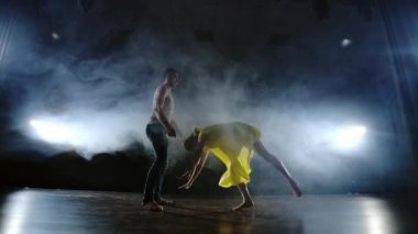 Zoom kamera, bir kadın dansçı ortağı omzuna atlar. Sahnede duman halinde akrobatik dans müzikali. Çağdaş Contemp