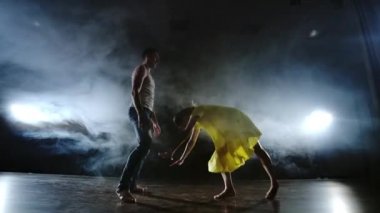 Zoom kamera, bir kadın dansçı ortağı omzuna atlar. Sahnede duman halinde akrobatik dans müzikali. Çağdaş Contemp