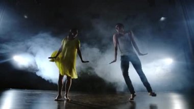 Bir erkek ve bir kadın birlikte kot pantolon komik bir dans ve duman sahnede sarı bir elbise dans. Müzikal