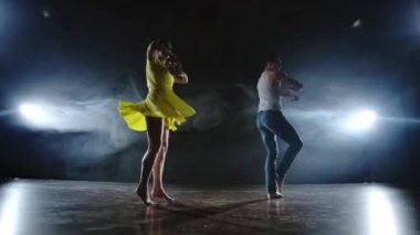 Bir erkek ve bir kadın birlikte kot pantolon komik bir dans ve duman sahnede sarı bir elbise dans. Müzikal
